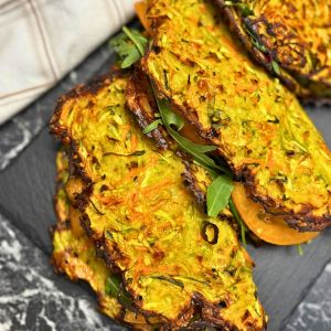 Close-up of crispy veggie wraps made from grated zucchini, carrots, and potatoes, baked until golden and filled with arugula and sliced tomato.