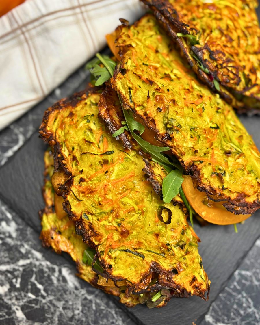 Close-up of crispy veggie wraps made from grated zucchini, carrots, and potatoes, baked until golden and filled with arugula and sliced tomato.