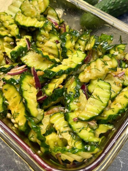 Garlic cucumber salad with red onion, dill, sesame seeds, and soy dressing in a glass container.