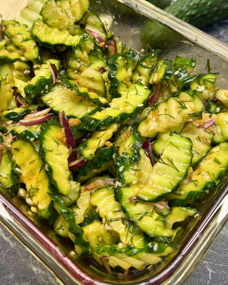 Garlic cucumber salad with red onion, dill, sesame seeds, and soy dressing in a glass container.