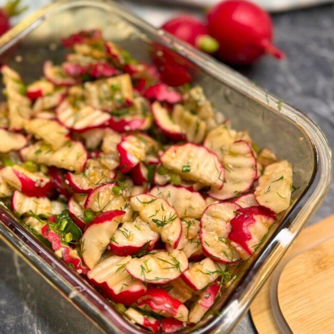 Glass container filled with quick pickled radish slices marinated in soy sauce, garlic, and herbs, topped with fresh dill and green onion.