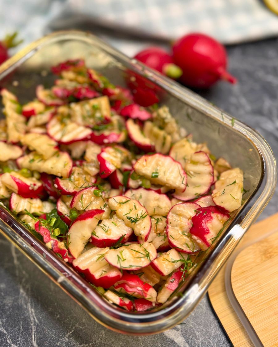 Glass container filled with quick pickled radish slices marinated in soy sauce, garlic, and herbs, topped with fresh dill and green onion.