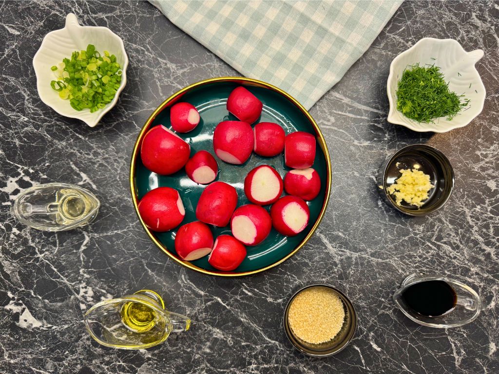 Flat lay of ingredients for quick pickled radish: halved radishes, chopped green onion, fresh dill, minced garlic, sesame seeds, soy sauce, apple cider vinegar, and olive oil arranged on a dark marble surface.
