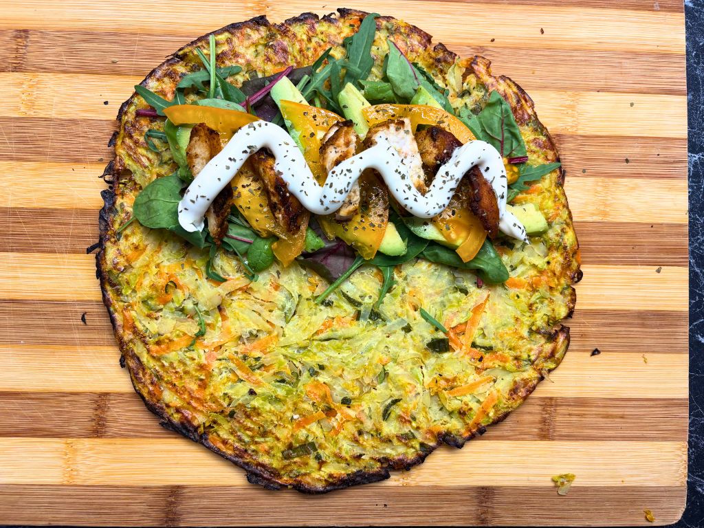 Baked crispy veggie wrap topped with mixed greens, avocado slices, yellow tomato, grilled chicken, and a swirl of yogurt sauce, ready to be folded.