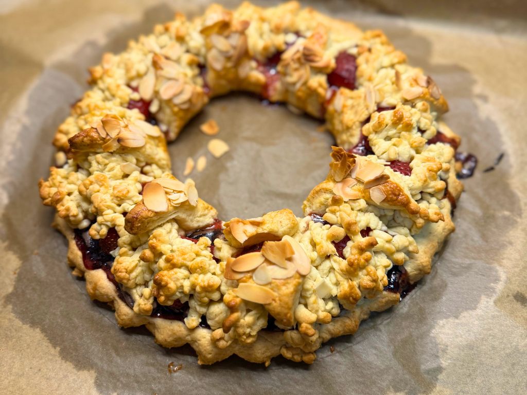 Freshly baked strawberry tart in a ring shape, topped with golden crumbles and sliced almonds, resting on parchment paper straight from the oven.