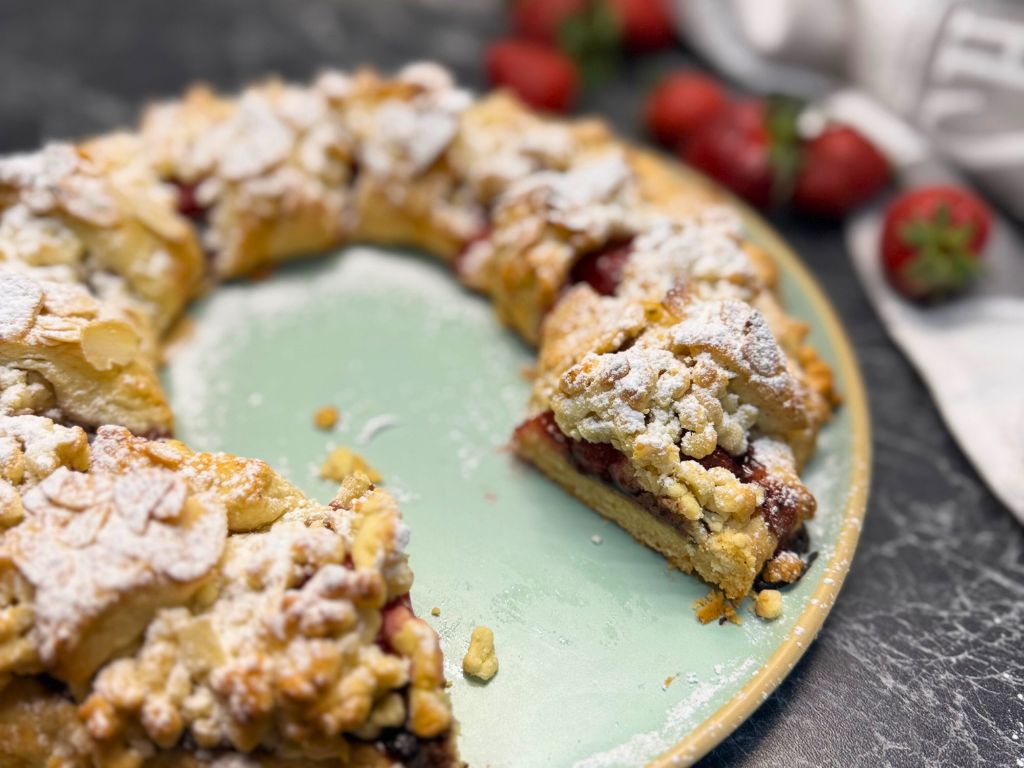 A close-up of a baked strawberry tart with a golden crust, filled with strawberries and chocolate, topped with powdered sugar, and served on a green plate.