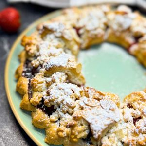 Close-up of a homemade strawberry tart with a golden, crumbly yogurt crust, topped with powdered sugar and baked into a decorative ring shape.