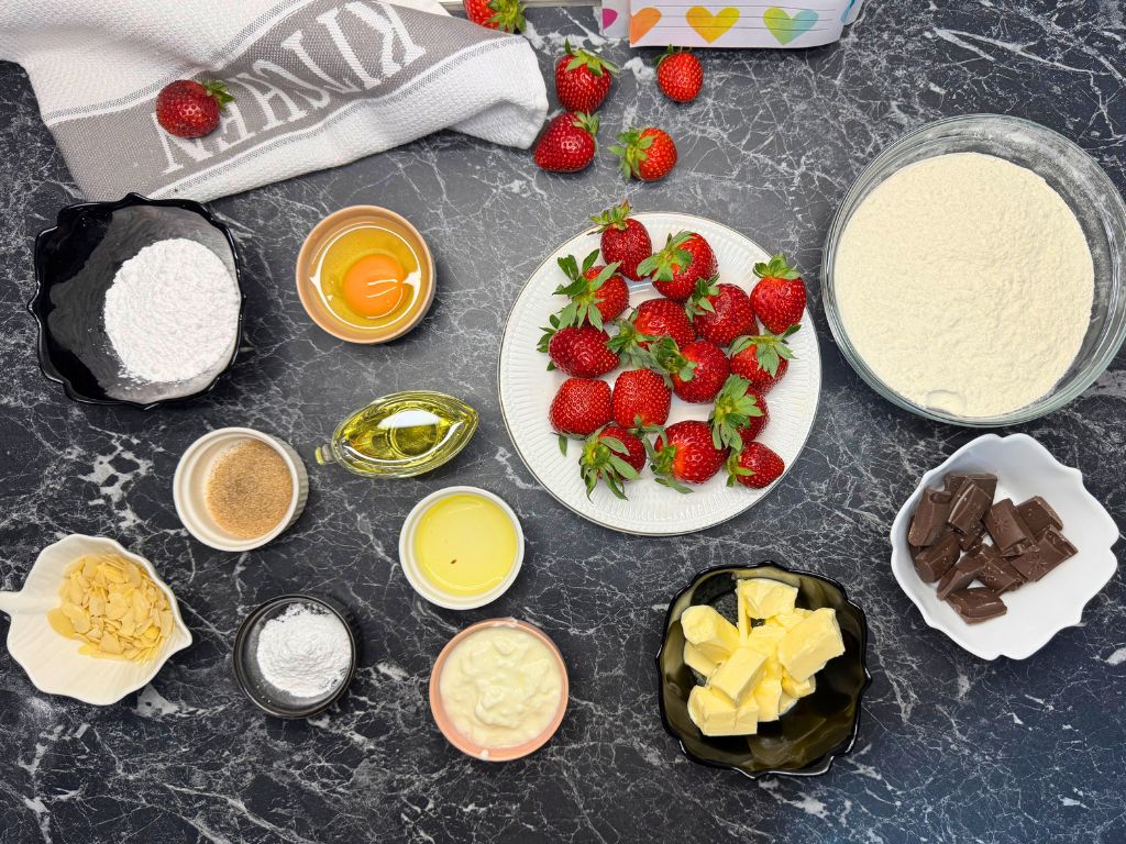 Top-down view of fresh strawberries and baking ingredients for a homemade strawberry tart, including flour, butter, chocolate, egg, yogurt, and powdered sugar.