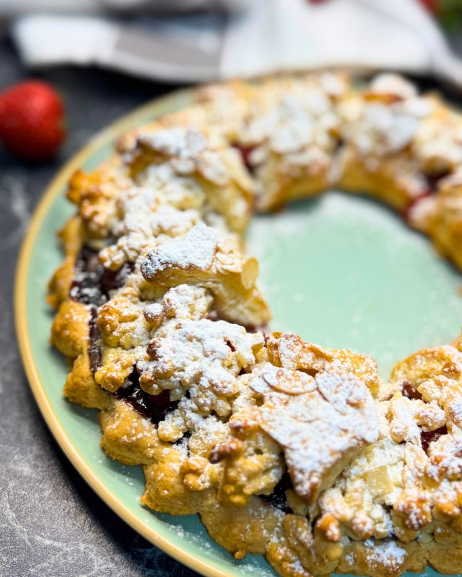 Close-up of a homemade strawberry tart with a golden, crumbly yogurt crust, topped with powdered sugar and baked into a decorative ring shape.