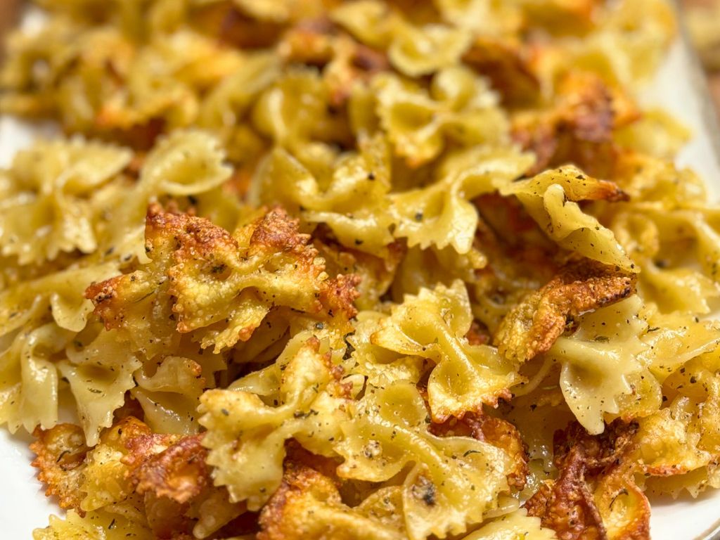 Extreme close-up of crispy bowtie pasta chips seasoned with herbs and Parmesan, showcasing golden edges and crunchy texture.