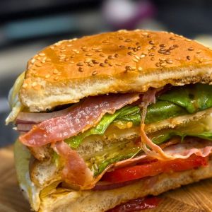 Close-up of a cheesy bacon egg burger cut in half, showing layers of bacon, lettuce, tomato, onion, cheese, and fluffy egg in a sesame bun.