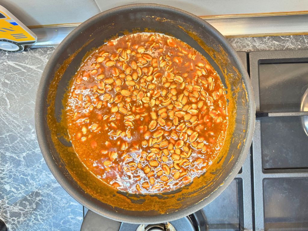 Caramel sauce simmering with roasted peanuts in a pan