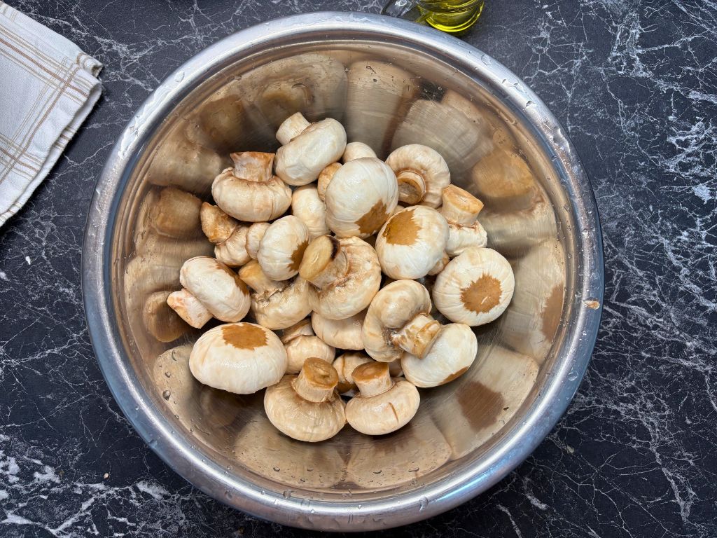 Freshly cleaned button mushrooms in a large stainless steel mixing bowl, ready for marinating.