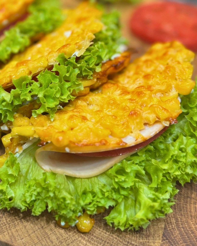 Close-up of a crispy corn cheese sandwich with lettuce, tomato, ham, and cream cheese