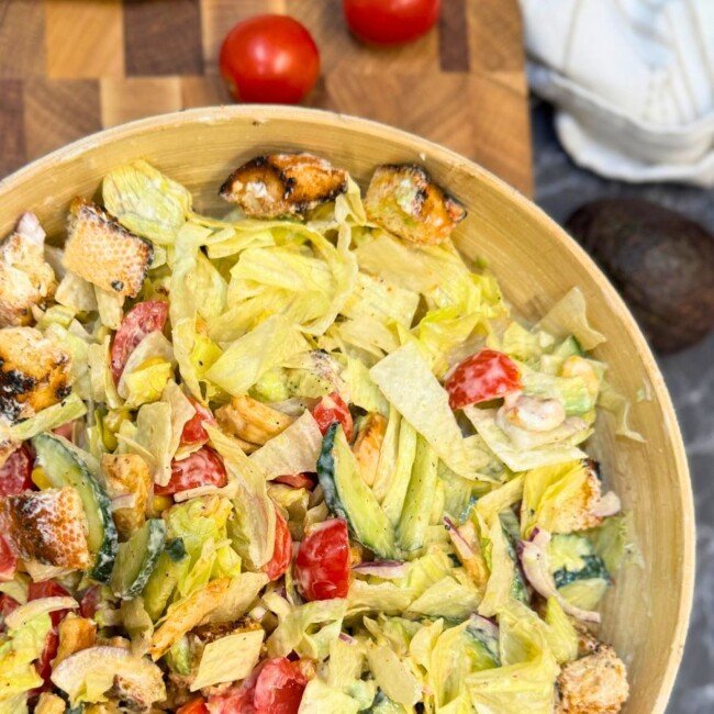 Healthy chicken salad with avocado, fresh vegetables, crunchy croutons, and creamy garlic dressing in a wooden bowl
