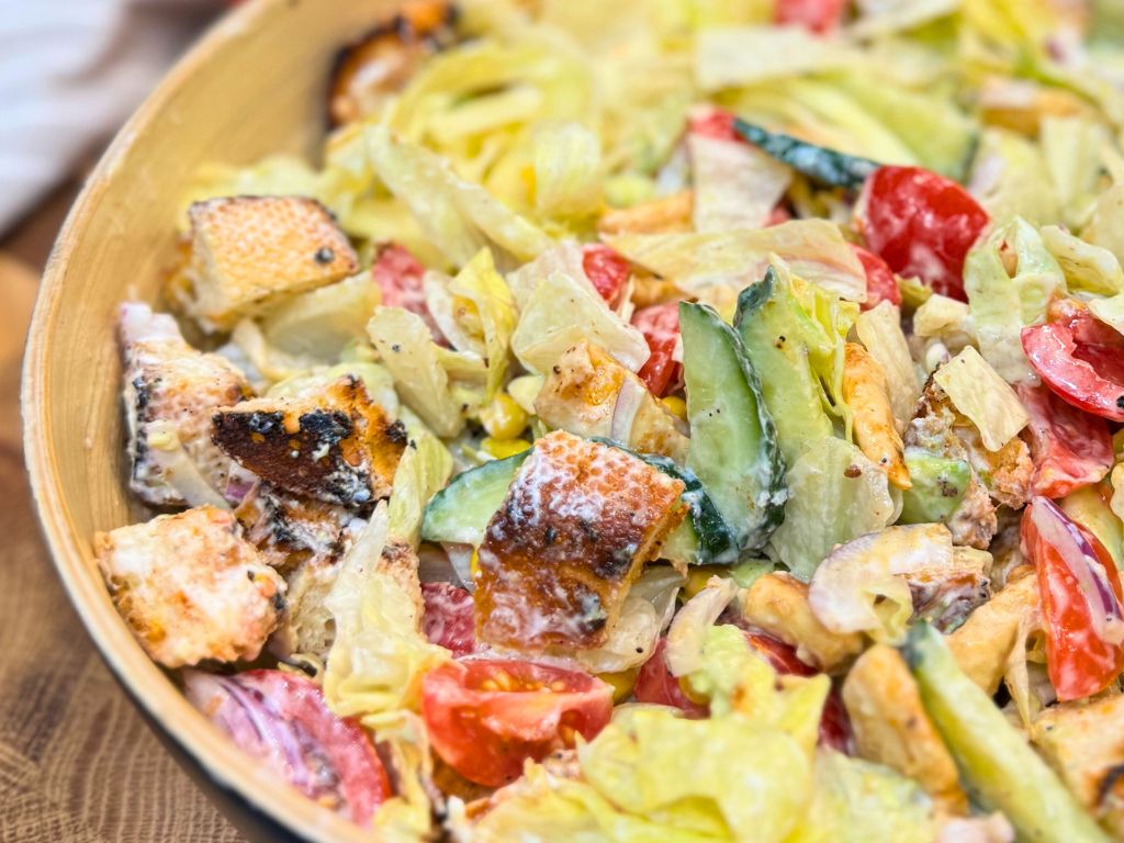 Close-up of healthy chicken salad with avocado, lettuce, cherry tomatoes, cucumber, grilled croutons, and creamy garlic dressing