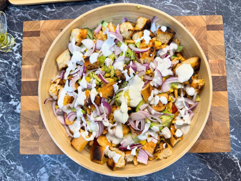 Bowl of healthy chicken salad with avocado, corn, cucumber, cherry tomatoes, red onion, crunchy croutons, and creamy garlic dressing