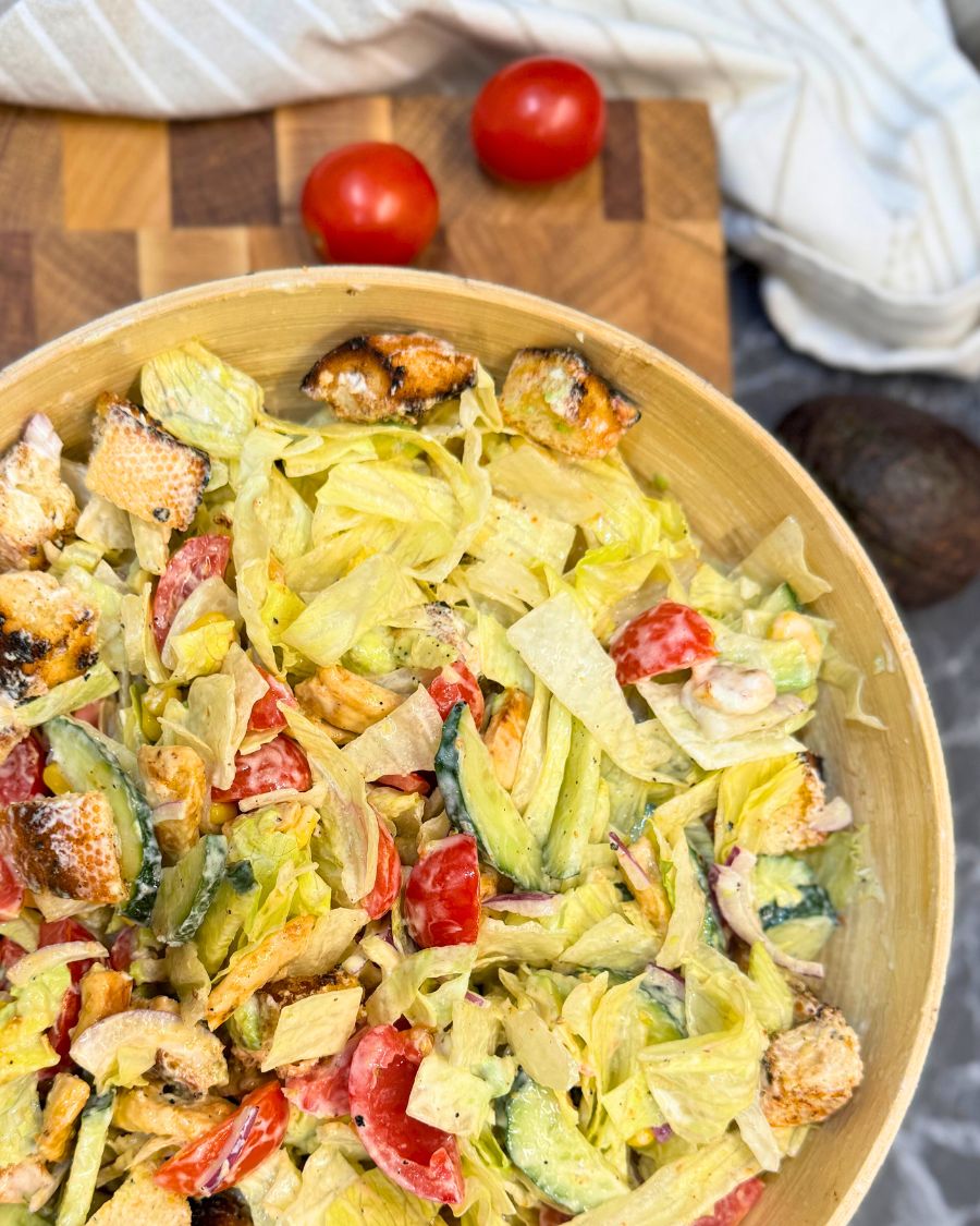 Healthy chicken salad with avocado, fresh vegetables, crunchy croutons, and creamy garlic dressing in a wooden bowl