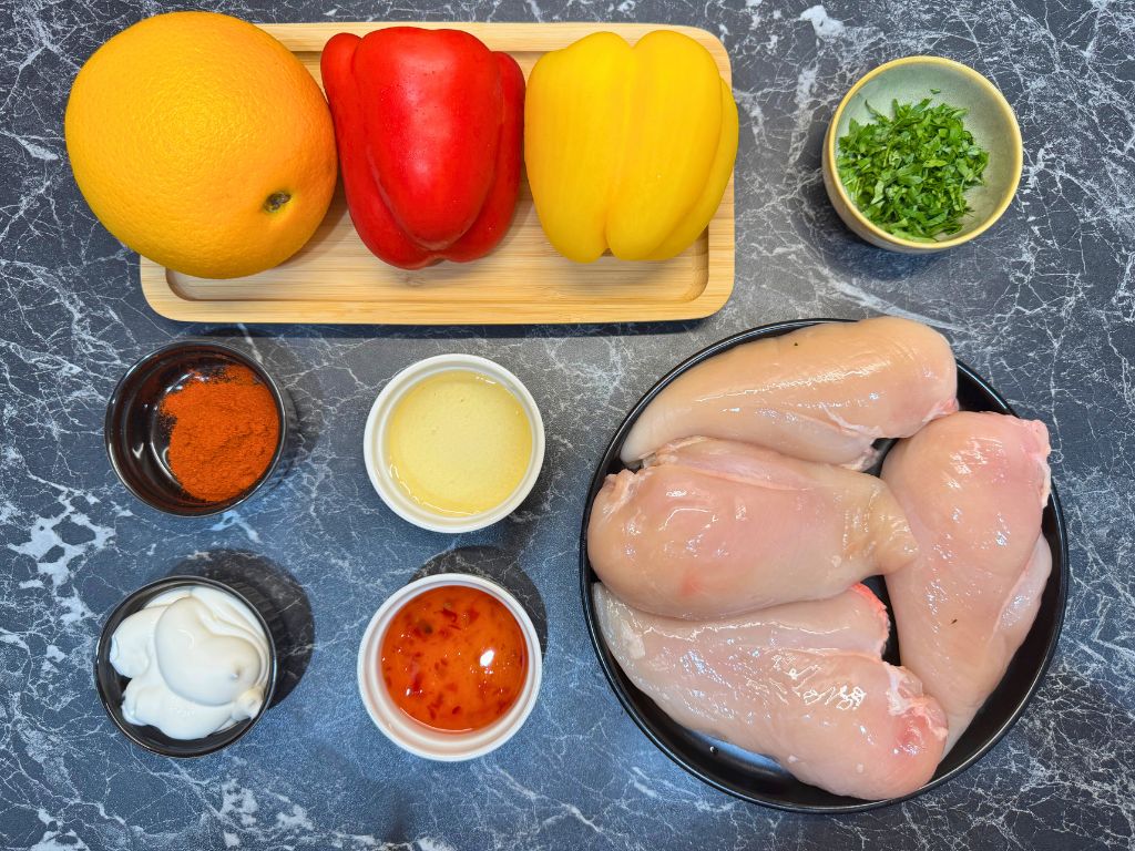 Fresh ingredients for air fryer chicken kebabs, including chicken breasts, orange, red and yellow bell peppers, parsley, smoked paprika, honey, mayonnaise, and sweet chili sauce.