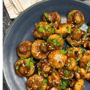 Roasted mushrooms glazed with soy sauce and honey, garnished with sesame seeds and fresh parsley on a dark plate.