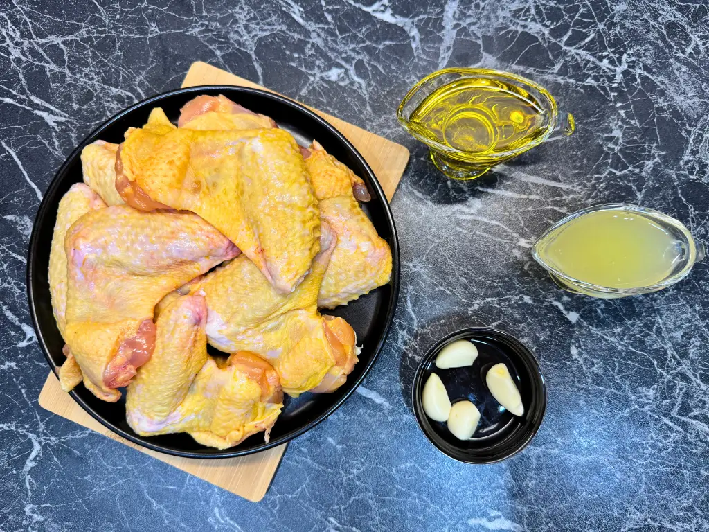 Raw chicken wings on a plate with garlic cloves, lemon juice, and olive oil for oven baked Lemon Fire Wings marinade