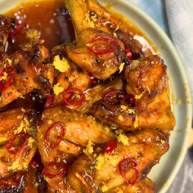 Plated oven baked lemon fire wings coated in sticky chili lemon sauce and topped with fresh lemon zest and red chili slices