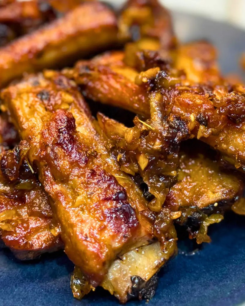 Close-up of tender beer braised pork ribs coated in caramelized onions and a glossy glaze.