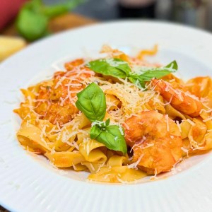 Creamy shrimp pasta with tomato sauce, Parmesan, and basil on a white plate.