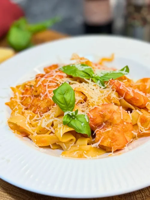 Creamy shrimp pasta with tomato sauce, Parmesan, and basil on a white plate.