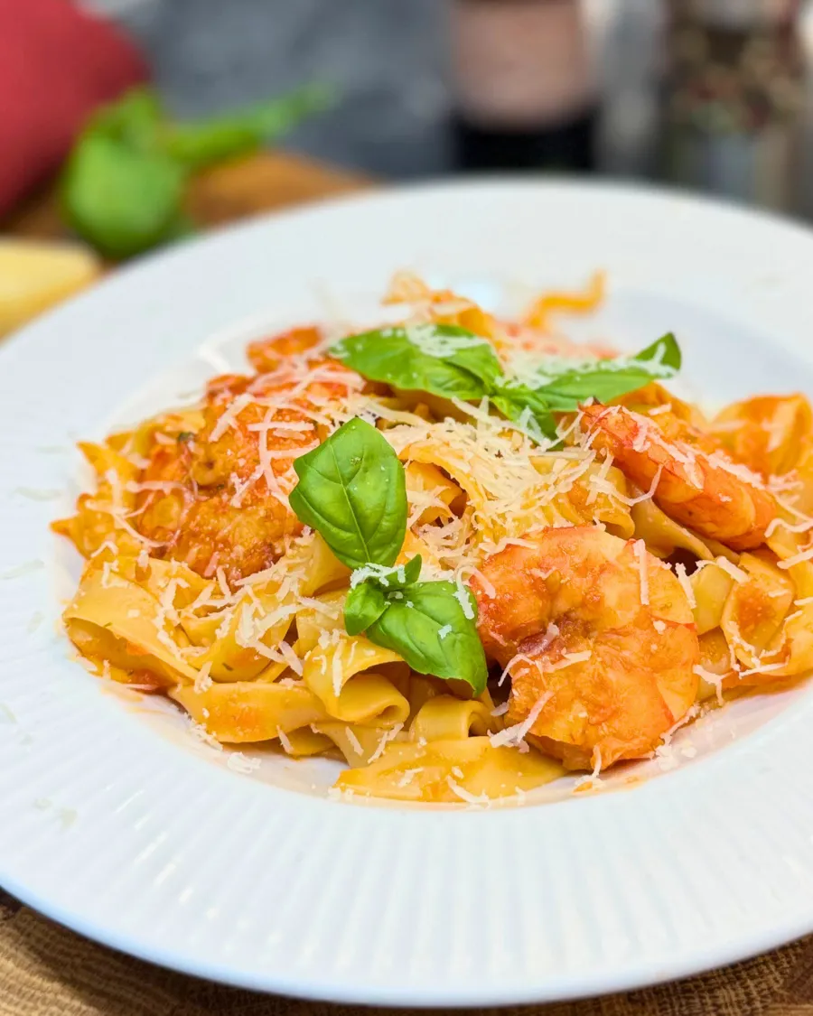 Creamy shrimp pasta with tomato sauce, Parmesan, and basil on a white plate.