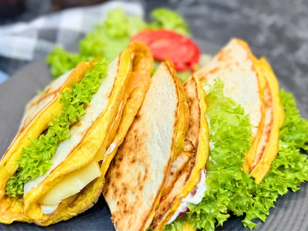 Finished chicken tortilla wraps with egg, cheese, lettuce, and tomato, stacked on a plate.