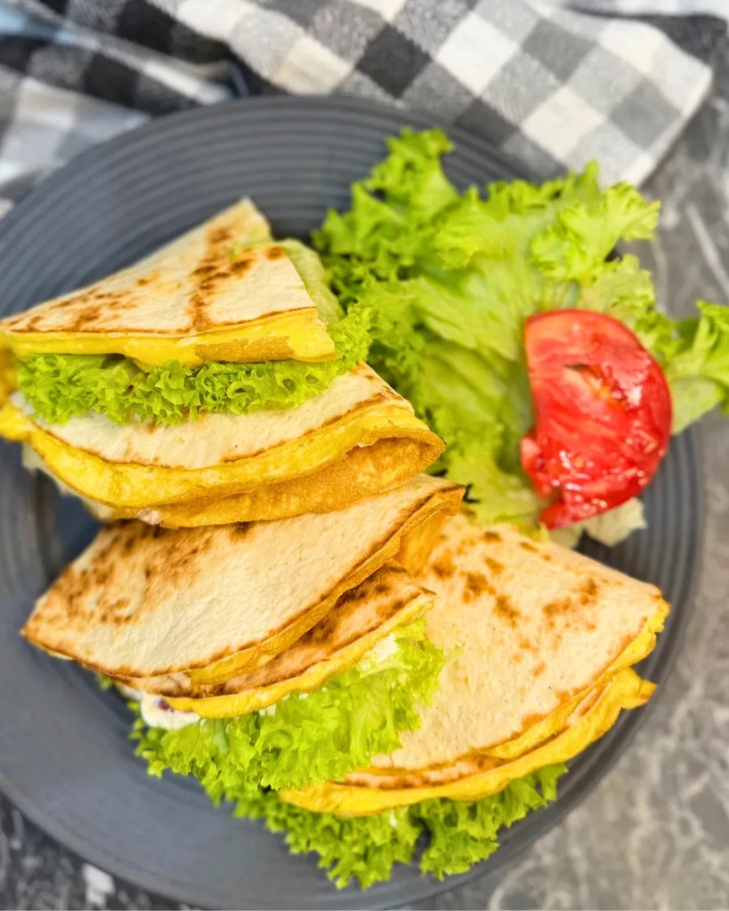 Overhead view of chicken tortilla wraps stacked on a plate with lettuce and tomato.