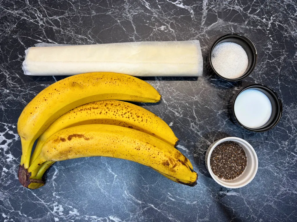 Bananas, puff pastry, sugar, milk, and chia seeds on a dark kitchen counter