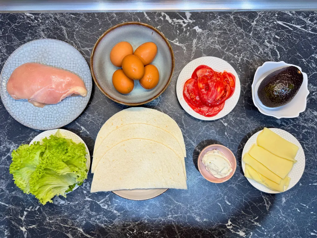 Ingredients for chicken tortilla wraps – chicken breast, eggs, tortillas, avocado, cheese, cream cheese, tomato, and lettuce.