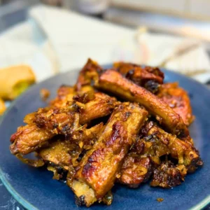 Juicy pork ribs braised in dark beer, stacked on a blue plate and topped with rich caramelized onion sauce.
