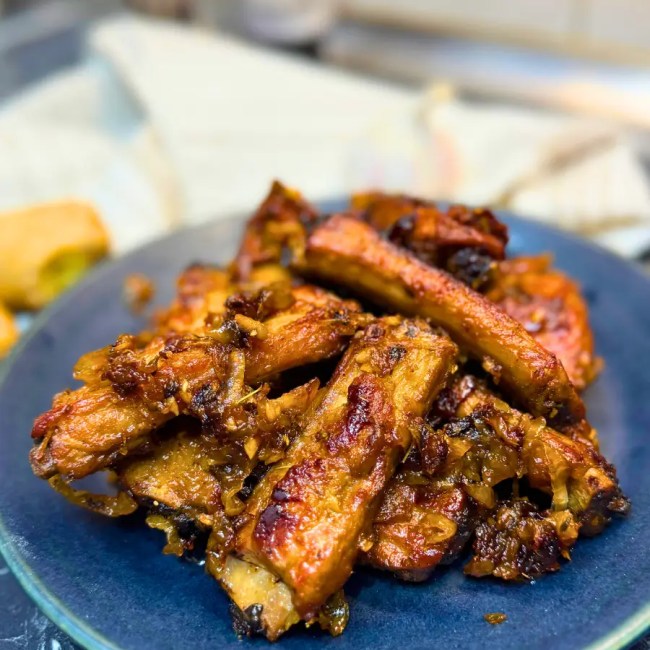 Juicy pork ribs braised in dark beer, stacked on a blue plate and topped with rich caramelized onion sauce.