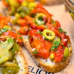 Fresh roasted pepper and olive salad in a glass bowl with slices of rustic bread in the background.