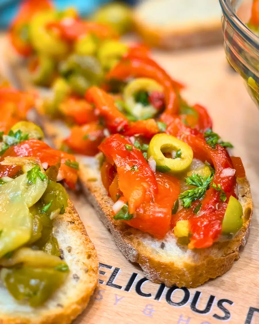 Fresh roasted pepper and olive salad in a glass bowl with slices of rustic bread in the background.