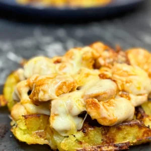 Close-up of crispy potato waffles topped with tender chicken pieces and melted cheese, golden and creamy on the edges.
