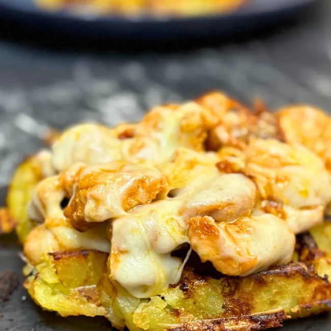 Close-up of crispy potato waffles topped with tender chicken pieces and melted cheese, golden and creamy on the edges.