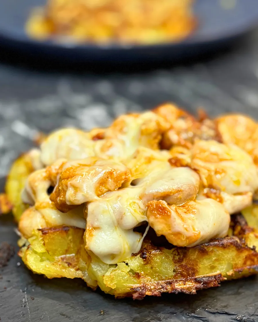 Close-up of crispy potato waffles topped with tender chicken pieces and melted cheese, golden and creamy on the edges.
