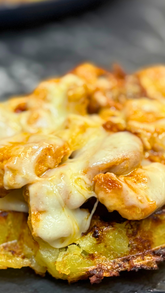 Close-up view of melted cheese and juicy chicken resting on a crispy, golden potato layer.