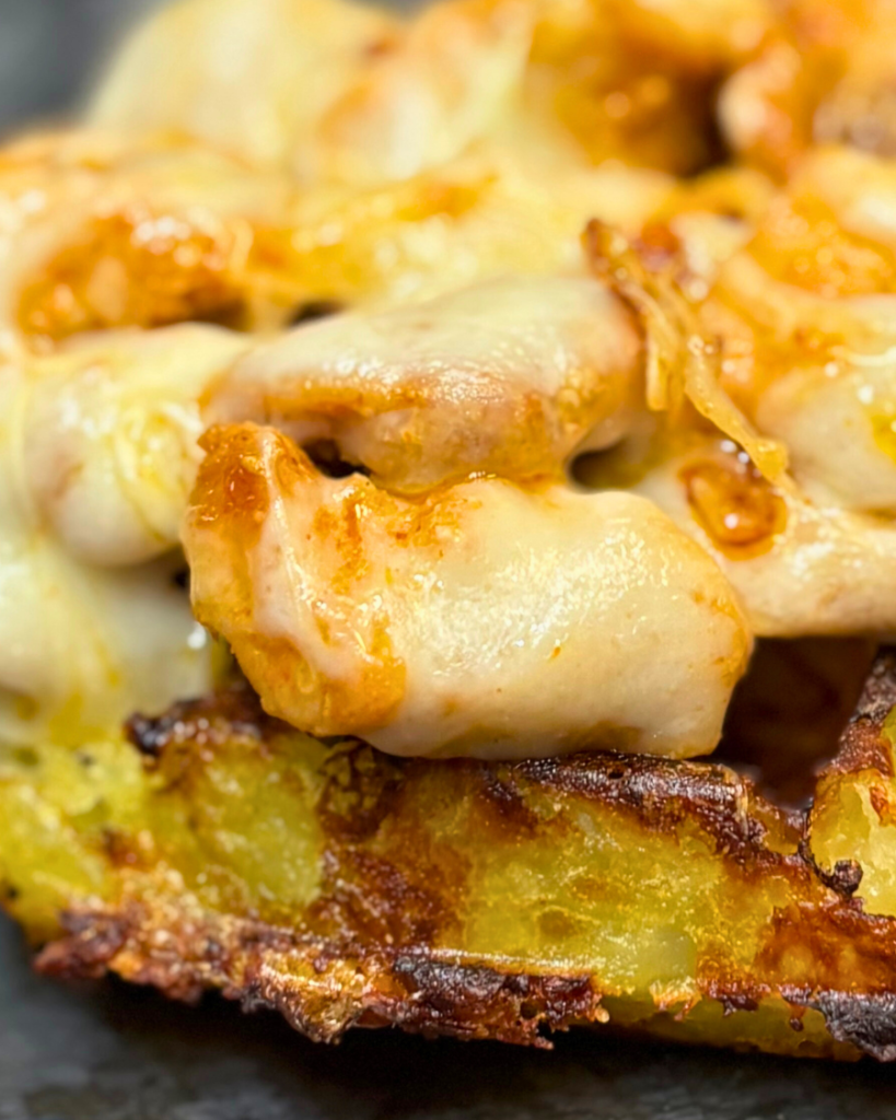 Close-up shot of juicy chicken pieces covered in melted cheese on top of a crispy, golden potato waffle.