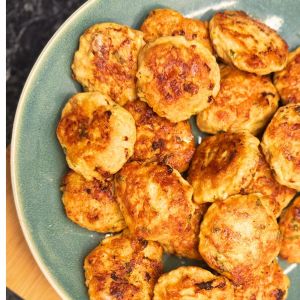 Golden chicken patties with melted cheese and fresh herbs, served on a green plate.
