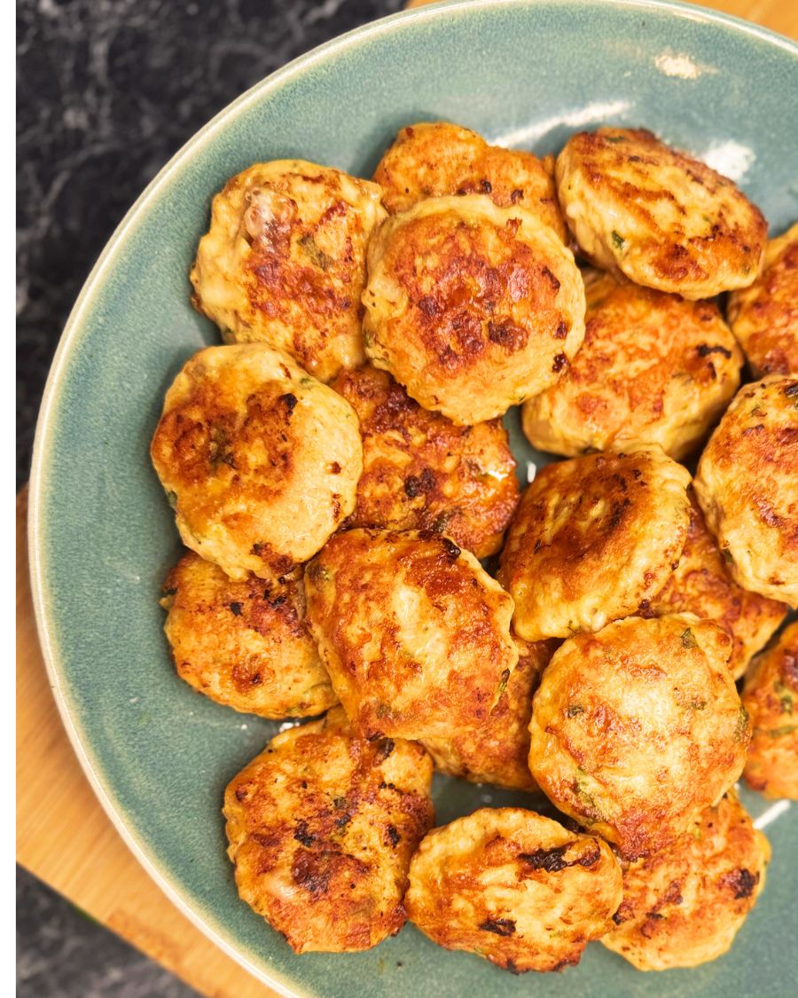 Golden chicken patties with melted cheese and fresh herbs, served on a green plate.
