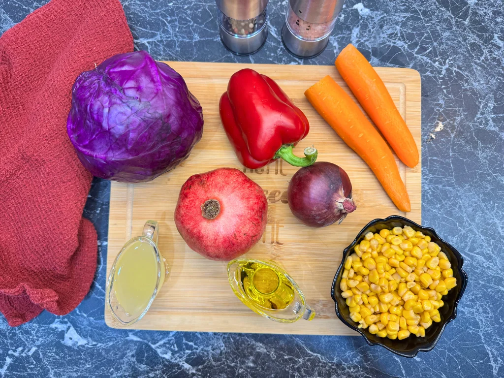 Ingredients for antioxidant raw vegetable salad including red cabbage, carrots, red bell pepper, pomegranate, corn, olive oil, and lemon juice