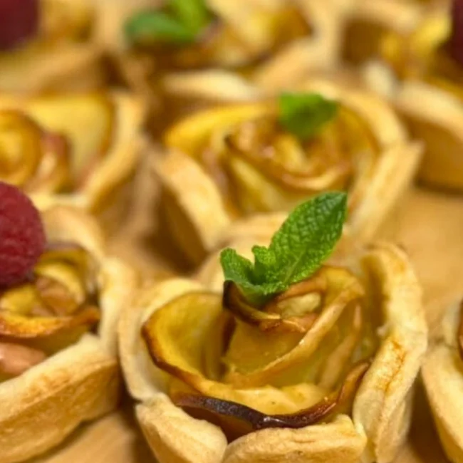 Detailed view of an apple rose tartlet with crisp puff pastry edges and a mint leaf garnish.