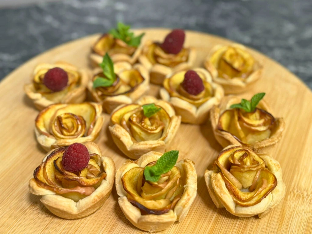 Golden apple rose tartlet made from thin apple slices rolled into a rose shape, topped with a fresh raspberry.