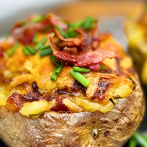 Close-up of a loaded baked potato with melted cheddar cheese, crispy bacon bits, and chives