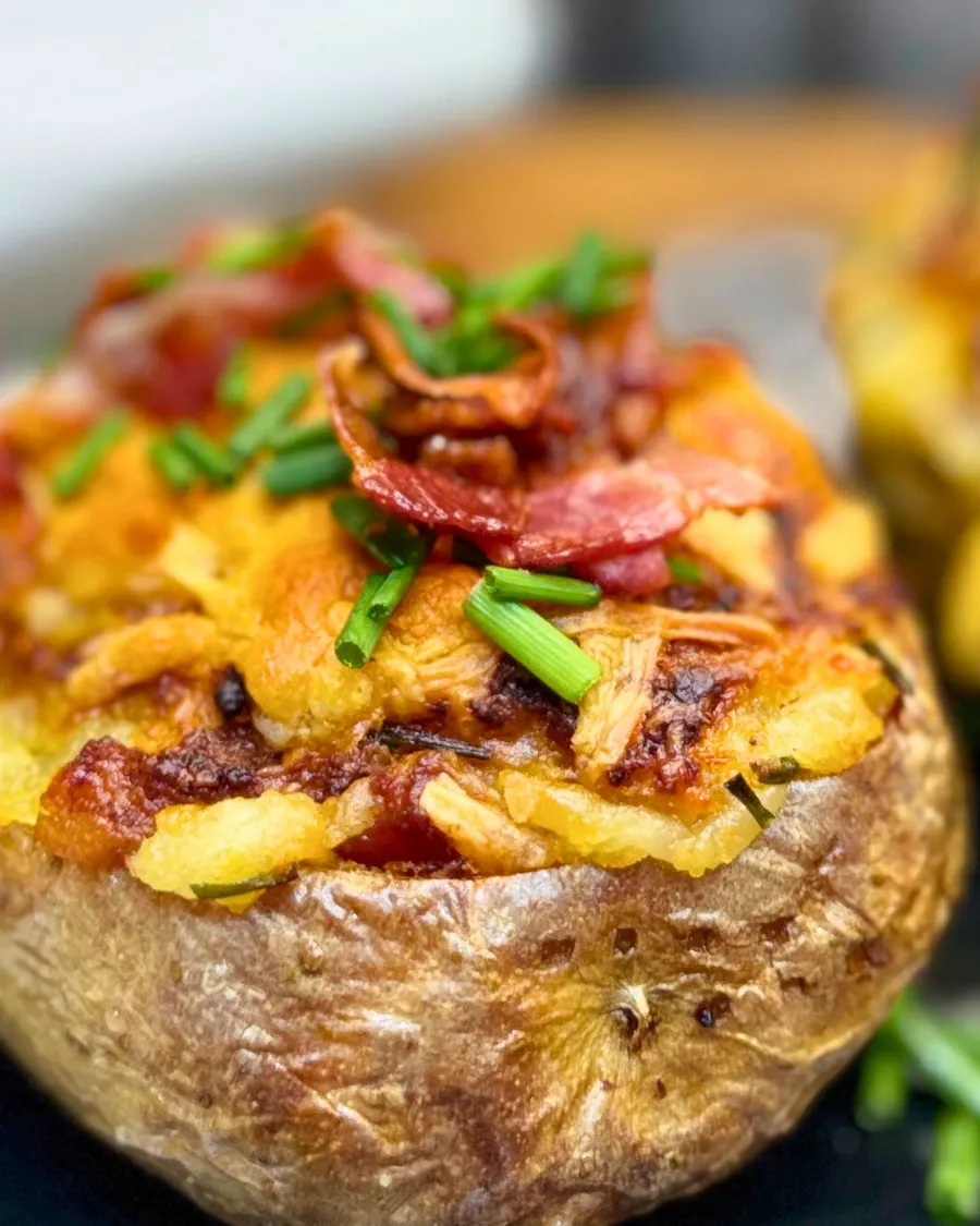 Close-up of a loaded baked potato with melted cheddar cheese, crispy bacon bits, and chives